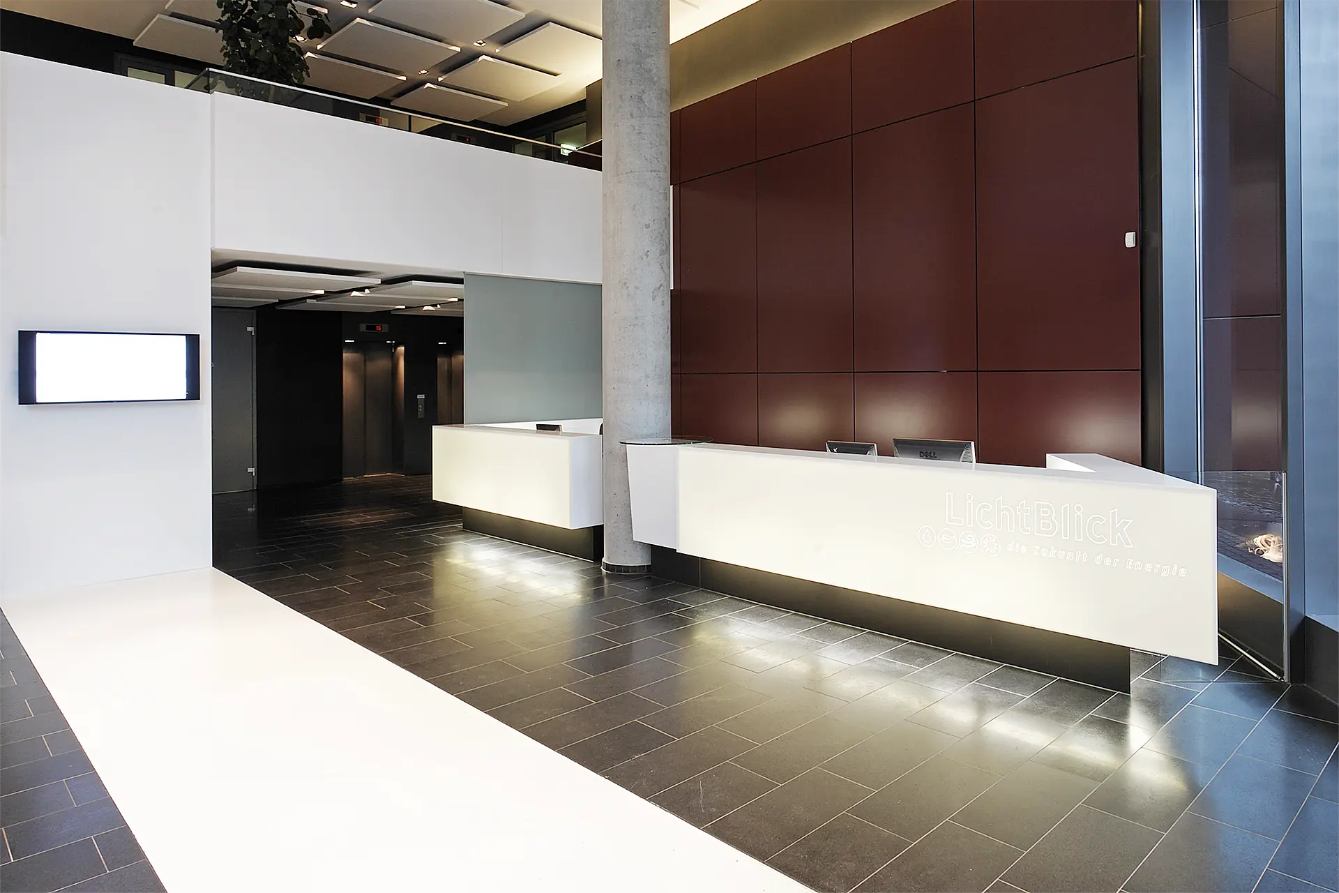 Weißer Empfangstresen aus Mineralwerkstoff steht in Halle vor braunroter Wand.