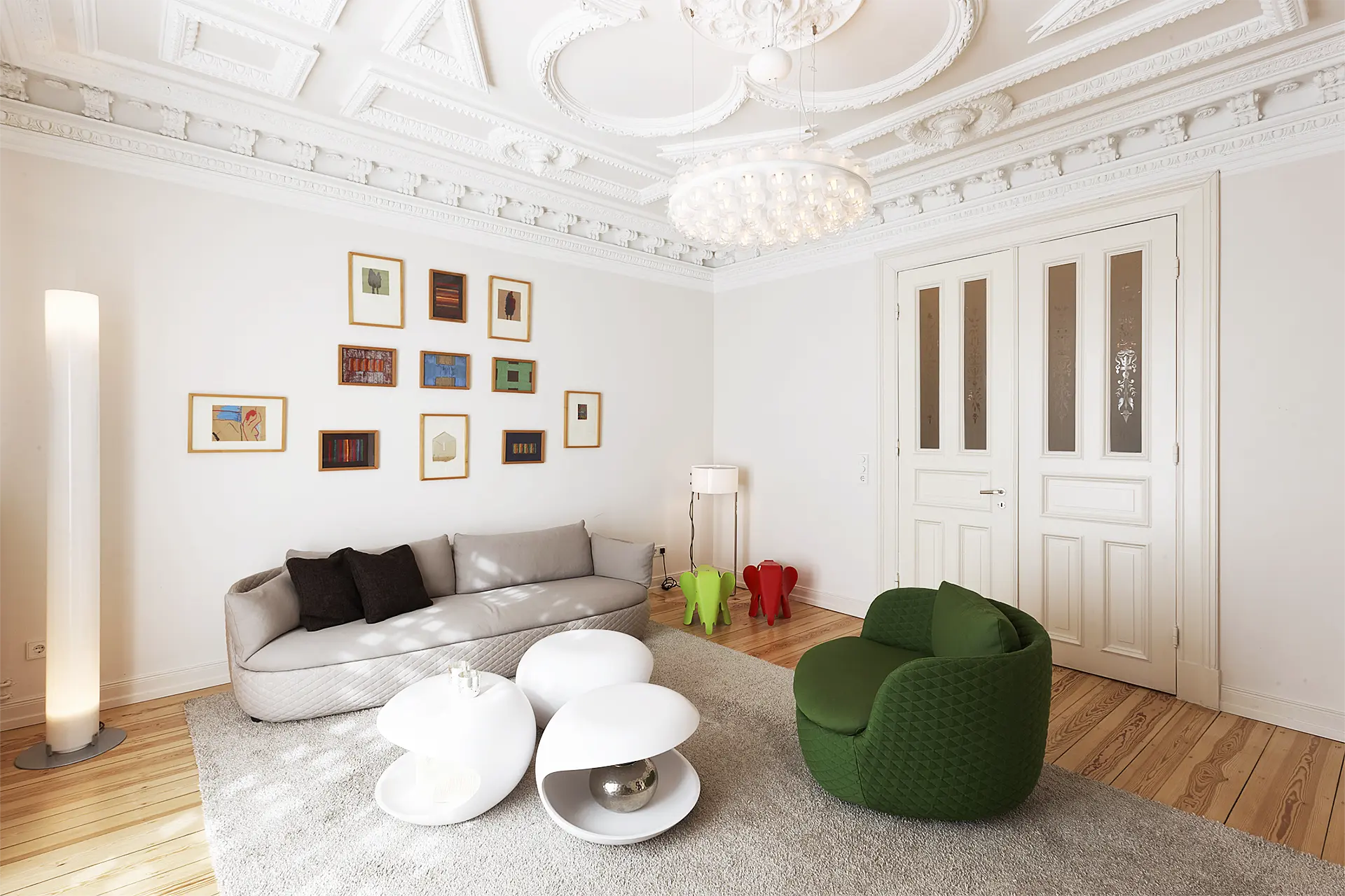 In einem Wohnzimmer mit Stuckdecke stehen ein graues Sofa, ein dunkelgrüner Sessel und weiße Tischelemente mit runden Formen.