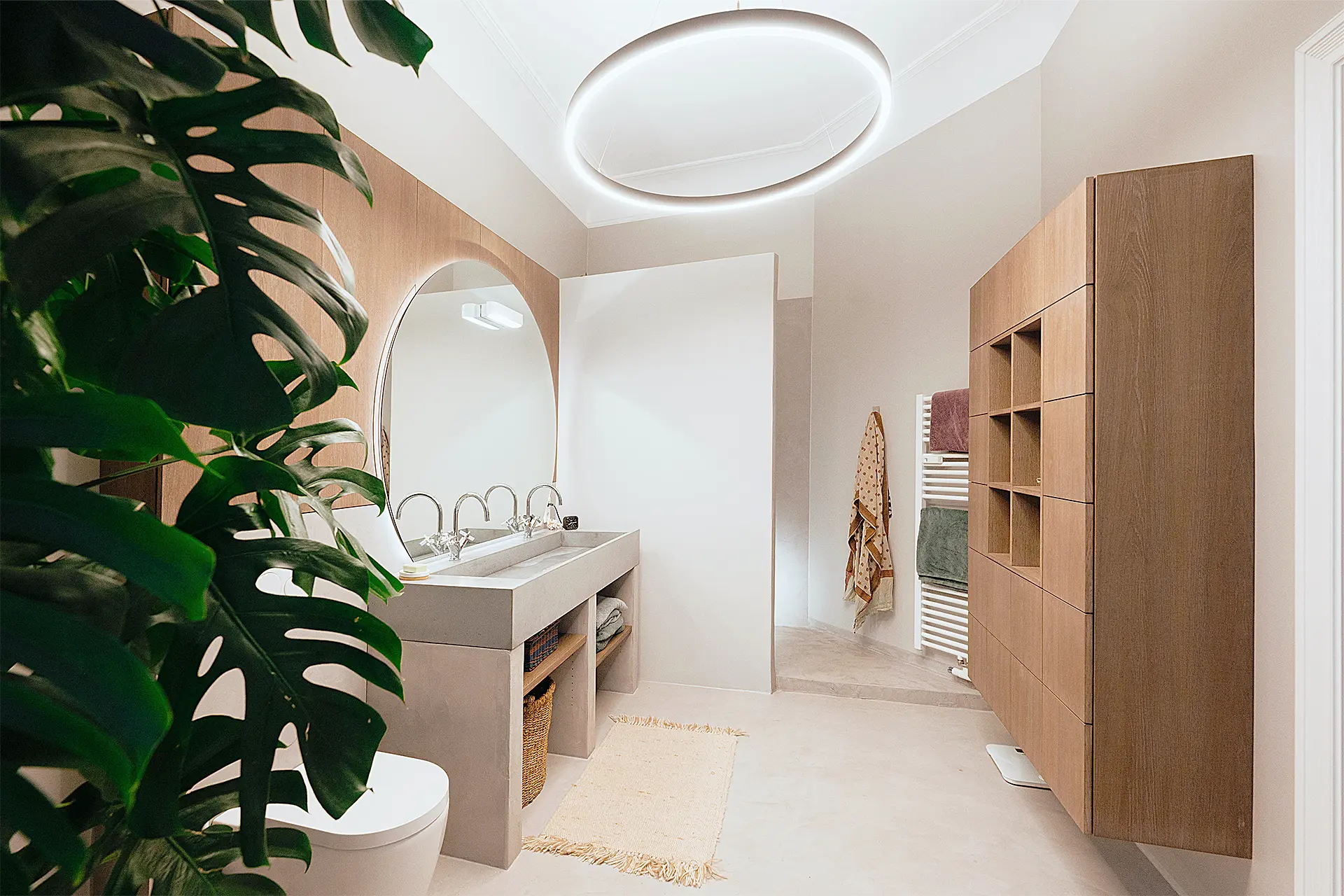 Bad mit kreisrunden Spiegel und Deckenleuchte verwendet den Werkstoff Mineralspachtel für Waschtisch und Boden ein.